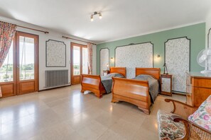 Een slaapkamer met twee houten bedden, een houten dressoir, een rieten stoel en een radiator.