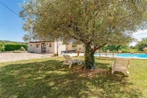 A villa with a swimming pool, two lounge chairs, and a tree in the yard.