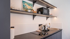 Moderni keittiö, jossa on mustat työtasot, mikroaaltouuni, vedenkeitin ja hylly, jossa on keittiötarvikkeita.