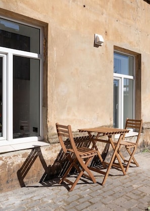 A wooden table and chairs outside a building with large windows. - Velvet Quartz Studio | Full Comfort (Rīga)