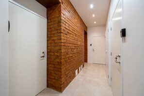 A hallway with a brick wall, white doors, and a tiled floor. - Velvet Quartz Studio | Full Comfort (Rīga)