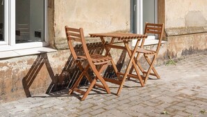 Ein Holz-Garnitur mit Tisch und Stühlen vor einem Gebäude mit strukturierter Wand und Fenstern.