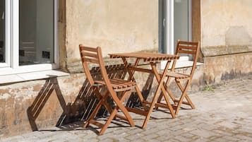 A wooden outdoor table and chairs set against a building with a textured wall and windows.