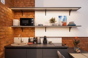 A kitchen with a brick wall, a black microwave, a coffee maker, and a sink. - The Hidden Gem | Smart & Quiet Studio (Riga)