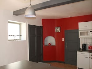 Una cocina con pared roja, techo blanco y una ventana con persianas.