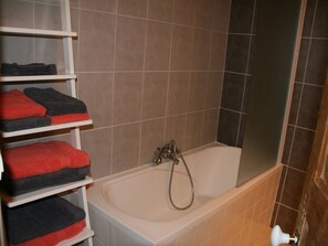 Ein Badezimmer mit einer Badewanne, Ablagen mit Handtüchern und einer Duschkabine.