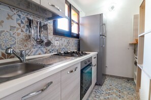 A kitchen with a sink, stove, and oven, tiled backsplash, and a refrigerator. - Golden Sunset - S'Archittu (S'Archittu)