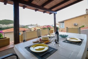 Une table dressée pour deux personnes, avec des assiettes, des couverts, une bouteille et des verres, donnant sur un paysage côtier.