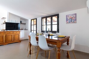 A dining area with a wooden table, white chairs, and a television on a wooden cabinet. - Golden Sunset - S'Archittu (S'Archittu)