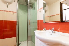 Une salle de bain avec une douche à parois de verre, un lavabo blanc et des murs recouverts de carreaux rouges.