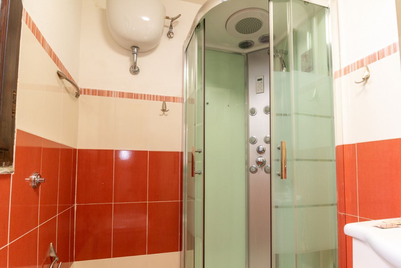 A bathroom with a glass-enclosed shower, a white sink, and red and white tiled walls.