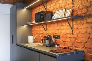 Eine Küche mit Backsteinwand, Spüle, Kaffeemaschine und Mikrowelle auf einem Regal.