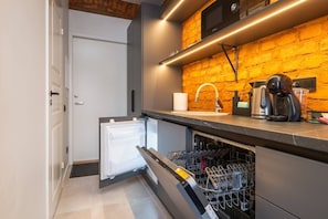 Eine kleine Küche mit Geschirrspüler, Kaffeemaschine und Mikrowelle vor einer Backsteinwand.