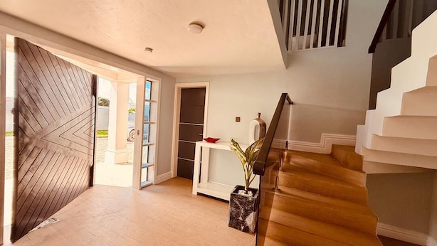 A spacious interior with a wooden staircase, a door with a geometric pattern, and a console table with a plant. - Zurano Villa – Your Spacious and Cosy Home Away from Home! (Dar es Salaam)