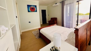 A bedroom with a bed, a bedside table with a lamp, a chair, a wardrobe, and a painting on the wall. - Zurano Villa – Your Spacious and Cosy Home Away from Home! (Dar es Salaam)