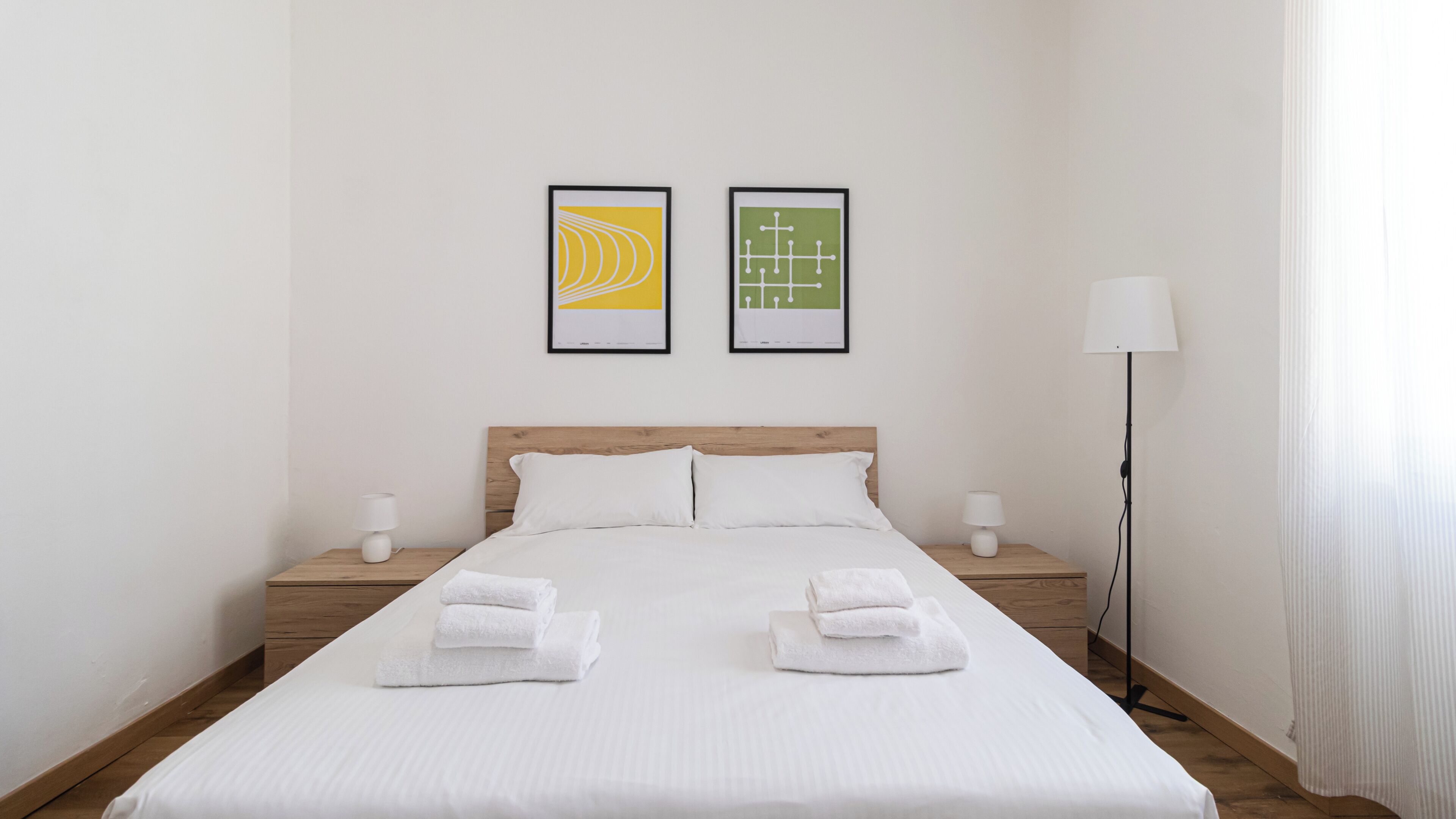 A hotel room with a bed, two nightstands, a lamp, and two framed pictures on the wall.
