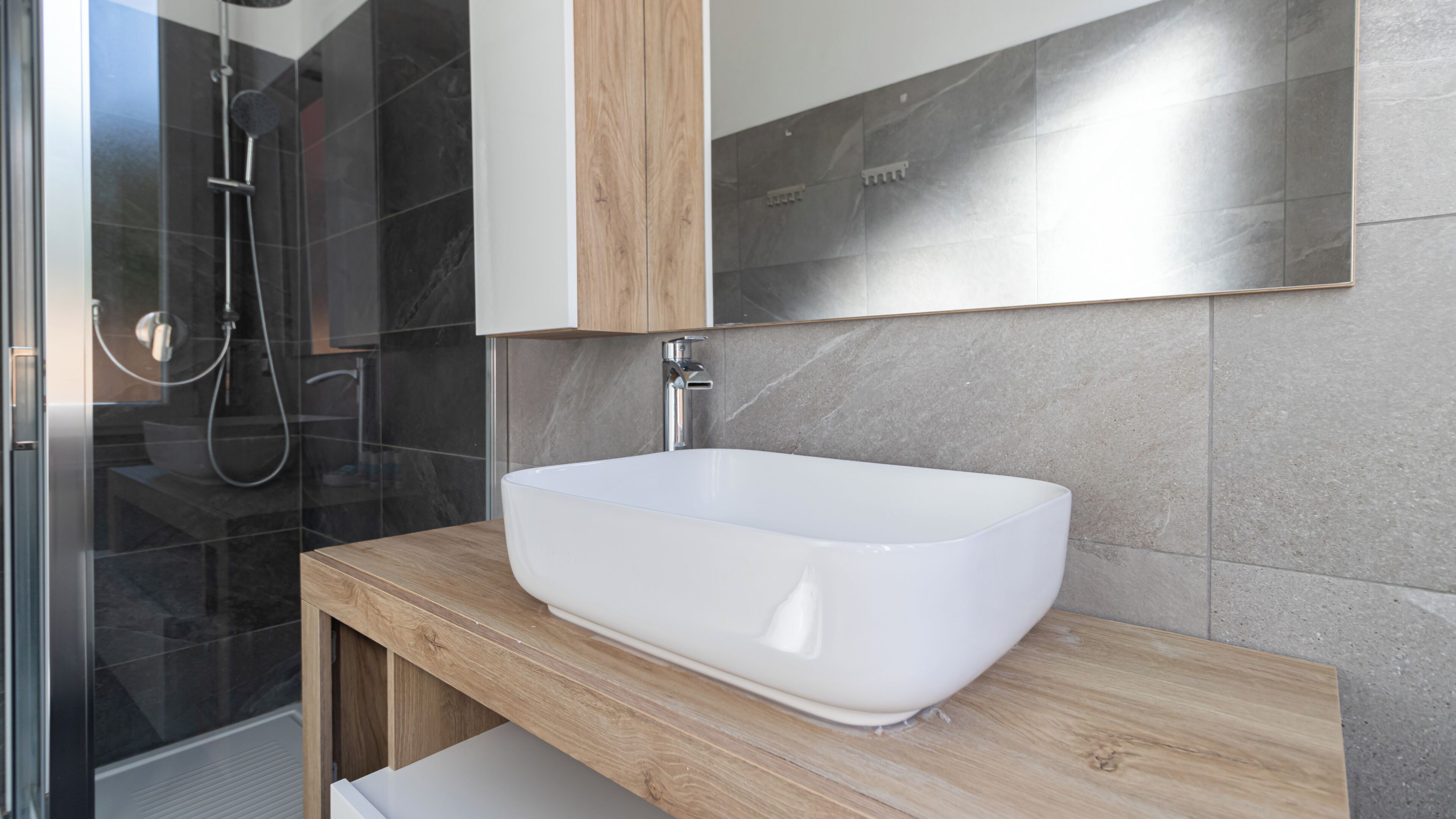 Ein modernes Badezimmer mit einem weißen Aufsatzwaschbecken, einer Duschkabine aus Glas und einem Holzbadezimmerunterschrank.