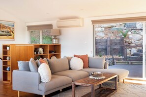 Ein Wohnzimmer mit einer Couch, einem Couchtisch, einem Holzregal und einem großen Fenster mit Blick auf einen Garten.