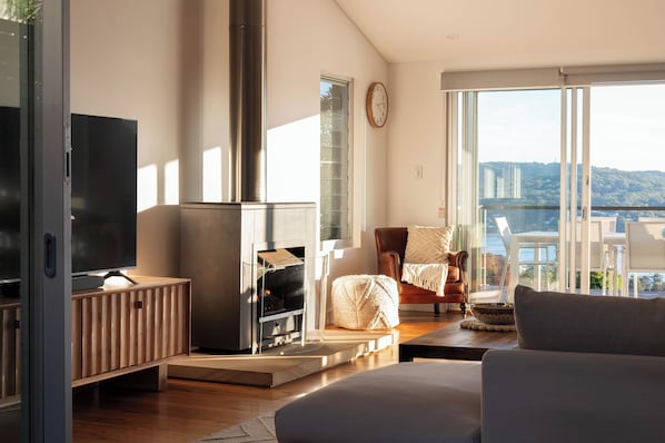 Ein modernes Wohnzimmer mit Kamin, Fernseher und Blick auf ein Gewässer.