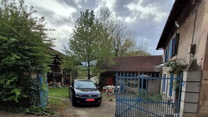 A paved driveway leading to a gated entrance with a car parked inside. - Ferme Berger-By & Le Nid, between the 2 lakes (Pressins)