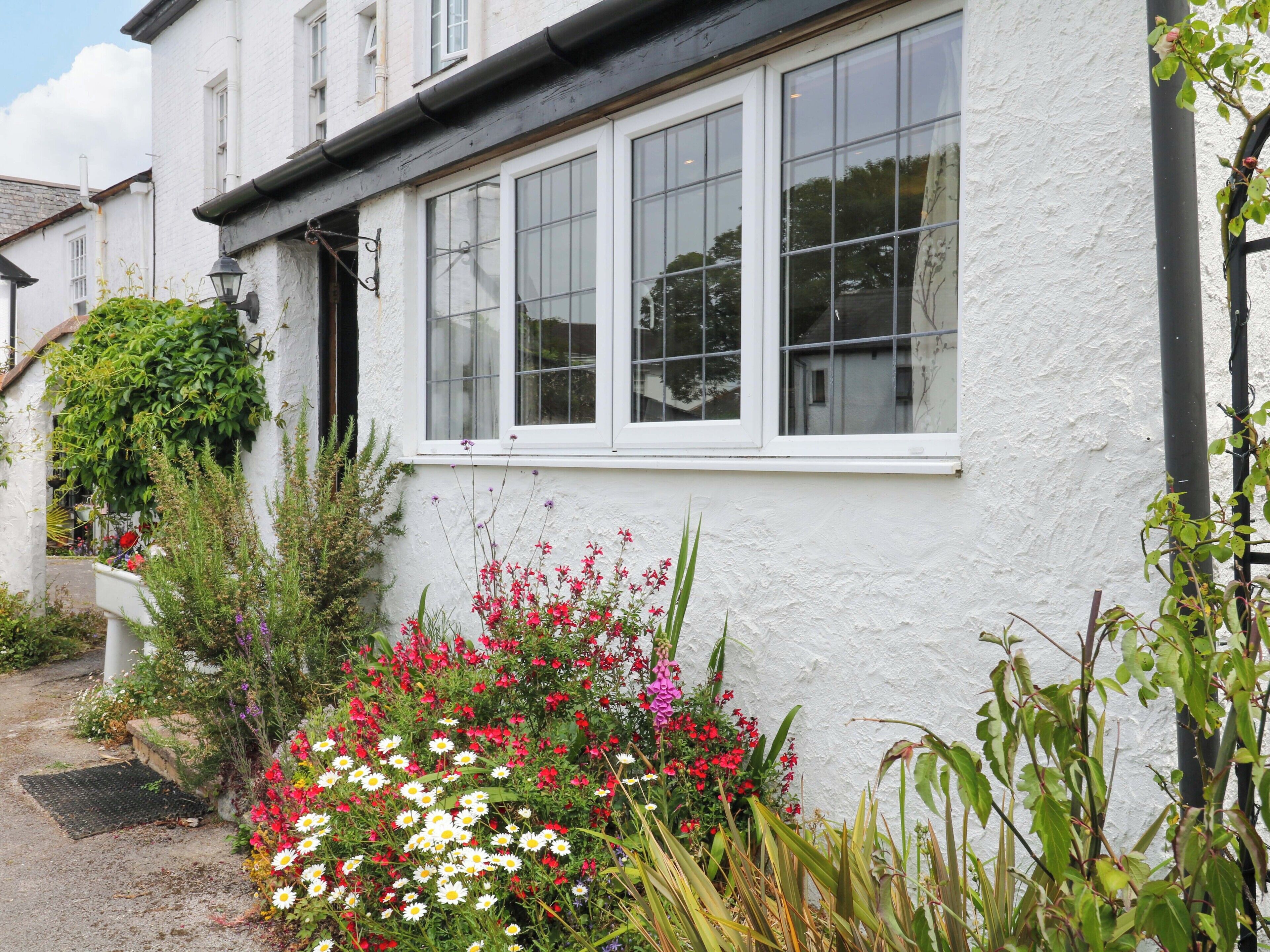 A white building with a window, a door, and a small garden with various plants and flowers.