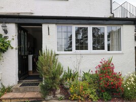 Un edificio blanco con marco negro en la ventana, una puerta y un pequeño jardín con diversas plantas y flores.