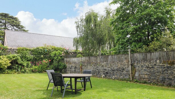 A grassy backyard with a stone wall, a wooden fence, and a table with chairs. - The Headmasters Quarters (Newton Abbot)