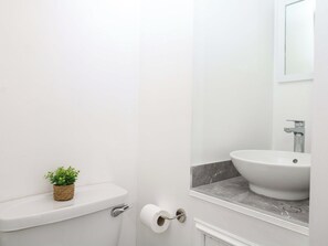 Ein Badezimmer mit Toilette, einer kleinen Pflanze, einer Toilettenpapierrolle, einem Waschbecken und einem Spiegel.