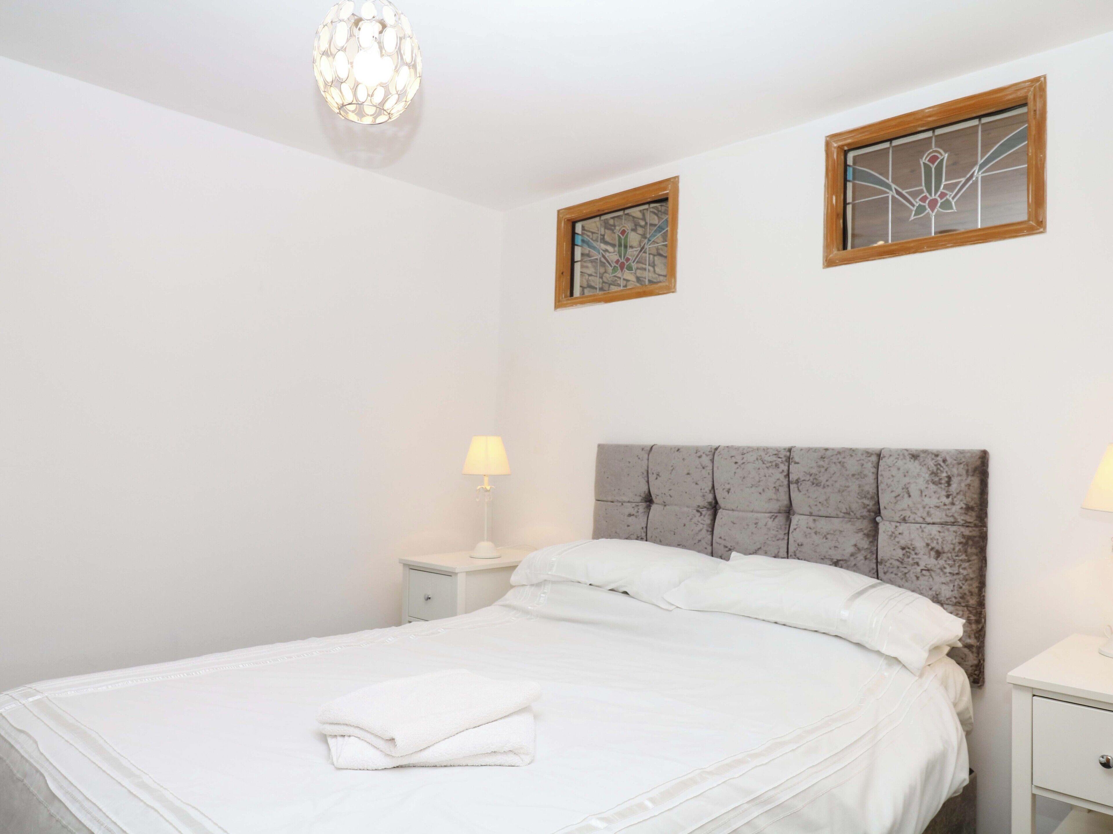 Een slaapkamer met een bed, twee bedlampen, een nachtkastje, een decoratieve plafondlamp en twee kunstwerken in lijsten aan de muur.