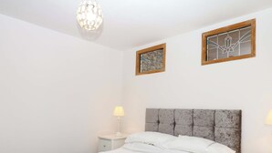A bedroom with a bed, two bedside lamps, a nightstand, a decorative ceiling light, and two framed artworks on the wall. - The Headmasters Quarters (Newton Abbot)