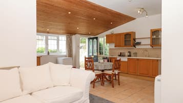 Una sala de estar acogedora con un sofá blanco, techo de madera y vistas a la cocina, que cuenta con armarios de madera y una ventana.