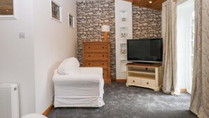 A room with a stone wall, a white chair, a wooden dresser, a TV on a wooden stand, and a radiator. - The Headmasters Quarters (Newton Abbot)