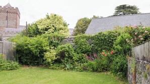 A grassy backyard with a stone wall, a wooden fence, and a variety of plants and flowers. - The Headmasters Quarters (Newton Abbot)
