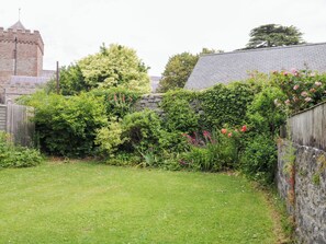 Ein grüner Hinterhof mit Steinmauer, Holzlattenzaun und verschiedenen Pflanzen und Blumen.
