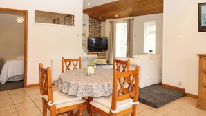 A dining area with a round table, wooden chairs, a potted plant, and a television in the background. - The Headmasters Quarters (Newton Abbot)