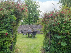 Ein Garten mit einer Steinmauer, einem Tisch mit Stühlen und üppigem Grün.