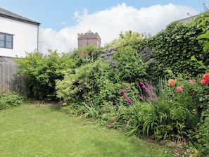 A garden with a variety of plants and flowers, a stone wall, and a building with a tower in the background. - The Headmasters Quarters (Newton Abbot)