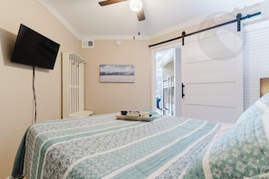 Ein Schlafzimmer mit einem Bett, einem Flachbildfernseher, einem Deckenventilator, einem Gemälde und einer Schiebetür.