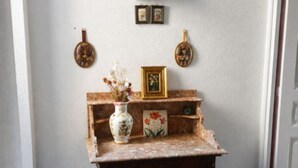 Habitación de esquina con alfombra azul, una mesa de madera con un florero y marcos de fotos, y una lámpara.