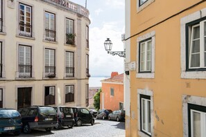 A street with parked cars, a building with balconies, and a lamp post. - Stunning Views | Authentic Lisbon Living (Lisbon)