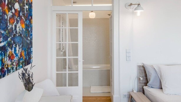 Un intérieur moderne avec une porte blanche donnant accès à une douche, un canapé blanc et un tableau abstrait aux couleurs vives.