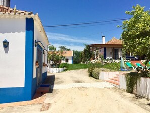 A residential street with houses, a clear sky, and a dirt path.