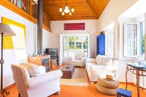 A spacious living room with a fireplace, white sofas, a television, and a large window.
