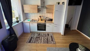 Eine kleine Küche mit Geschirrspüler, Backofen und Spüle. Ein Fenster mit Vorhängen, ein Blumentopf und ein Holzboden.