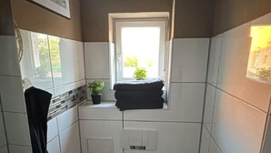 Ein kleines Badezimmer mit Toilette, Handtuchhalter, Heizkörper und Fenster.