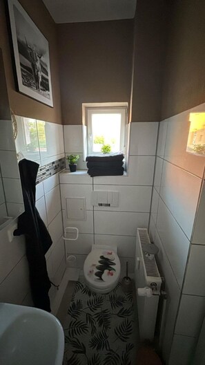 Ein kleines Badezimmer mit Toilette, Handtuchhalter, Heizkörper und Fenster.