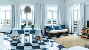 A room with a dining table, chairs, a sofa, and a TV stand. - Floating Over the Sado | Arrábida, Beaches & Town (Setúbal)