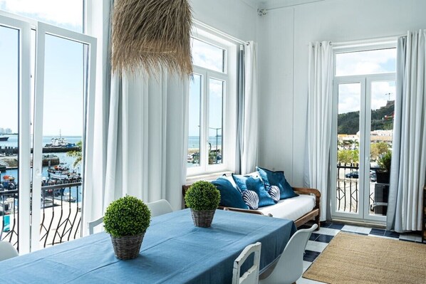 Ein Balkon mit Blick aufs Meer, ein Tisch mit blauer Tischdecke und eine Sitzecke mit blauen Kissen.