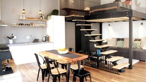 A modern kitchen with a dining area, a staircase, and a living room with a sofa. - Modern Coastal Ocean Breeze Studio | Beach & Town (Setúbal)