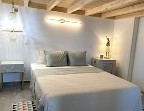 Um quarto com cama, mesas de cabeceira, um candelabro e uma luminária na parede.